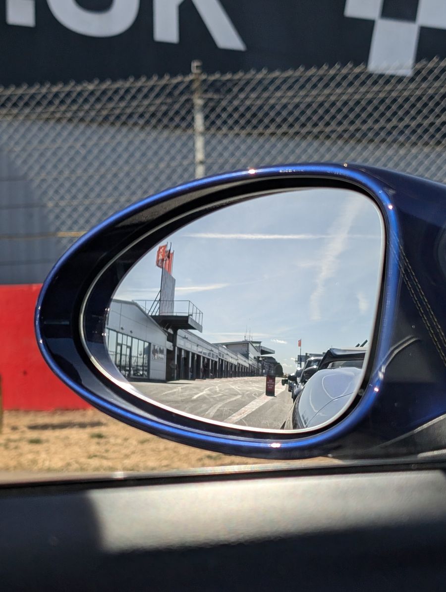 The Donington Park pit lane reflected in the wing mirror of a blue Porsche GT4