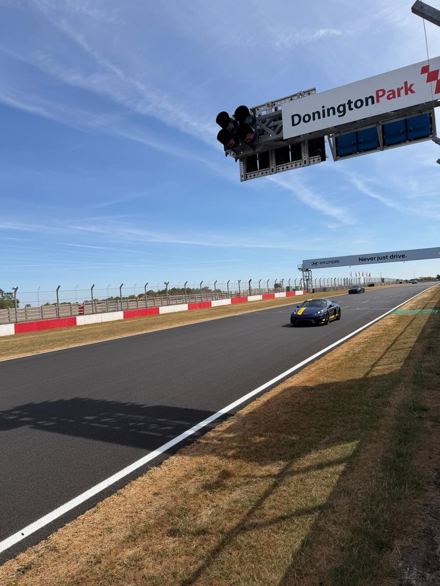 A blue Porsche GT4 passing under the Donington Park start gantry