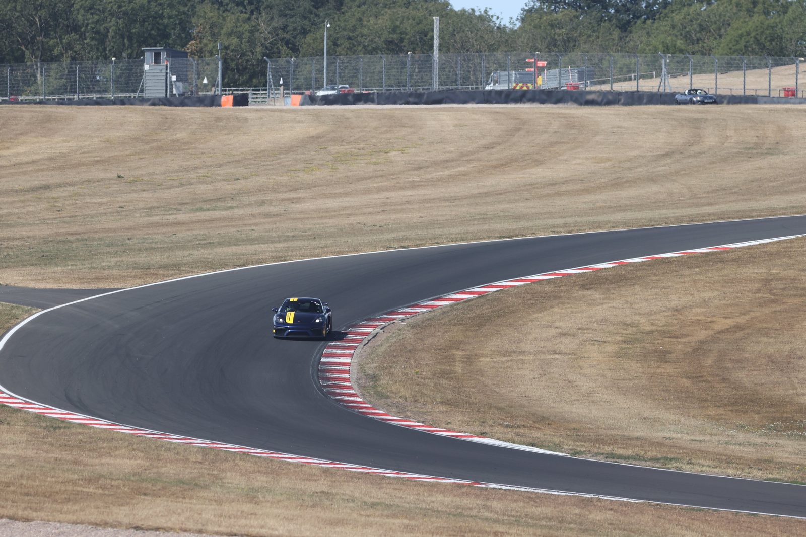 A blue Porsche GT4 with a yellow stripe through the Craner Curves at Donington Park