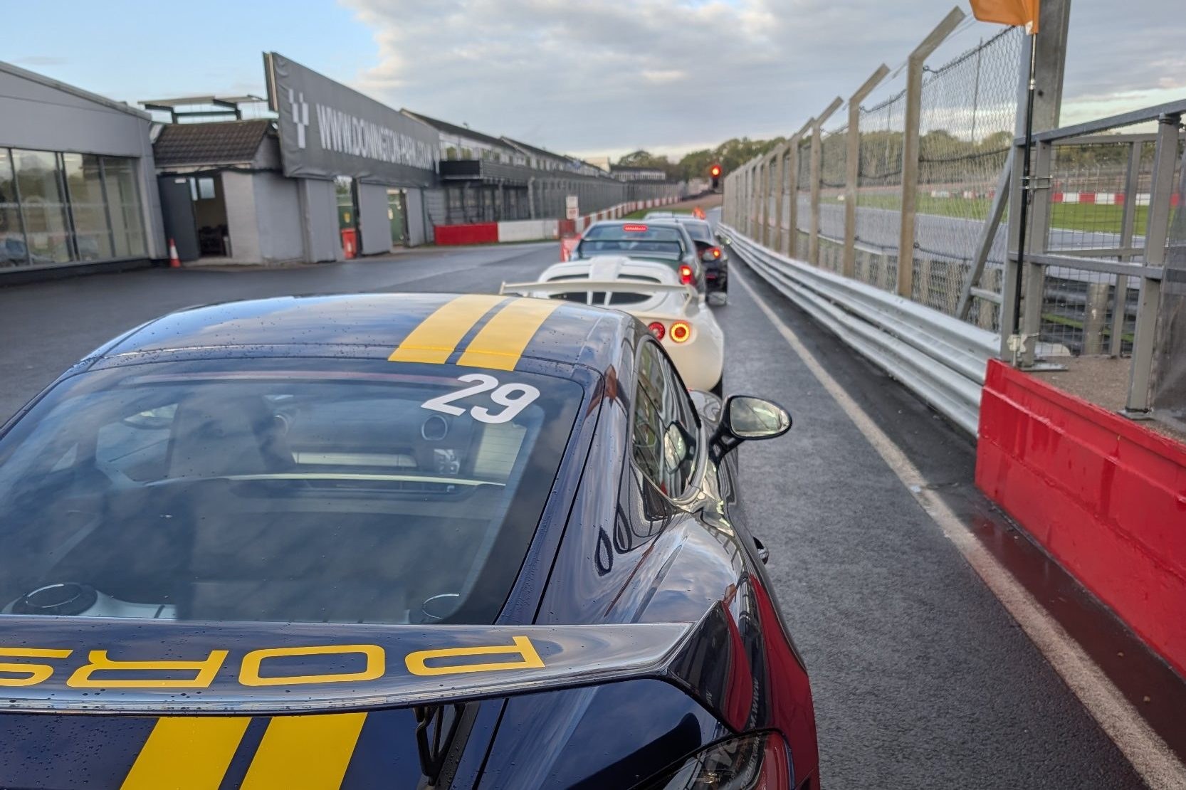 A blue Porsche 718 Cayman GT4 with race number 29 queuing in the wet pit lane at Donington Park, ready to go out with RaceLineApp.ai coaching live.