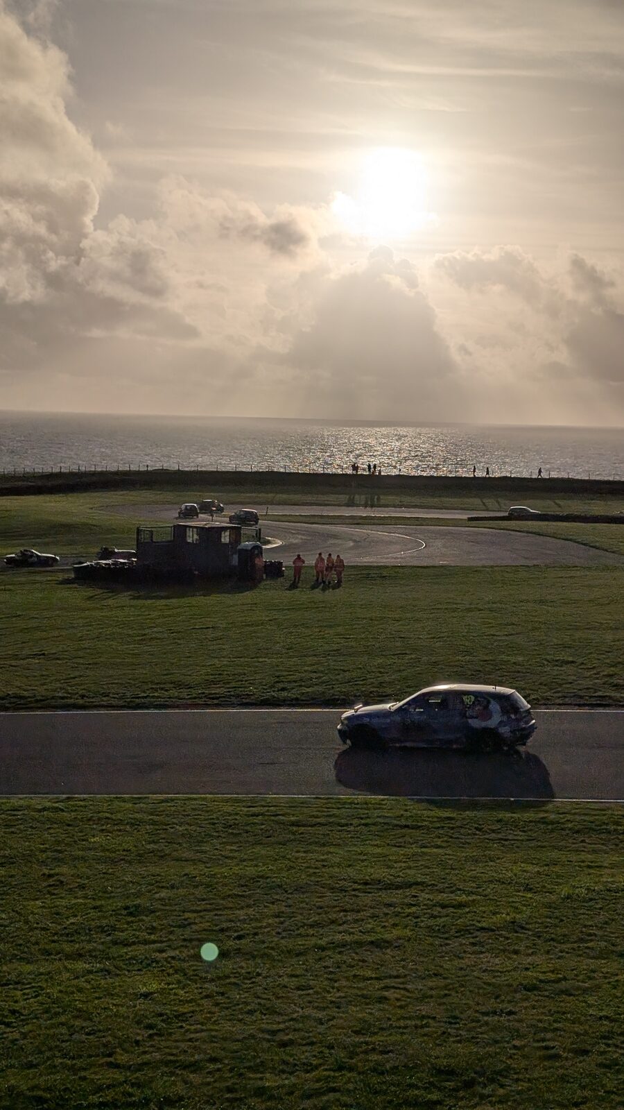 A race car on Anglesey Circuit at dusk, the Irish Sea and a breaking sky beyond.